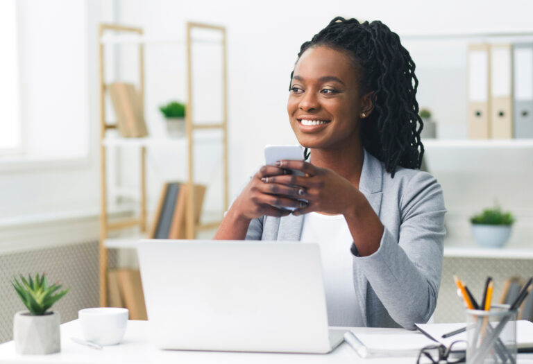 Woman of color in front of a laptop and cell phone with a relaxed and happy expression