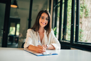 woman in a white blouse smiling, writing down a list on a clipboard